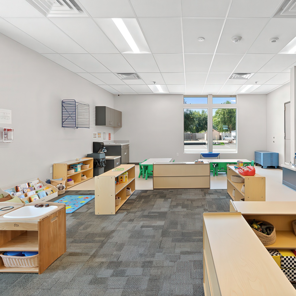 Classroom with shelves, tables, and green chairs.