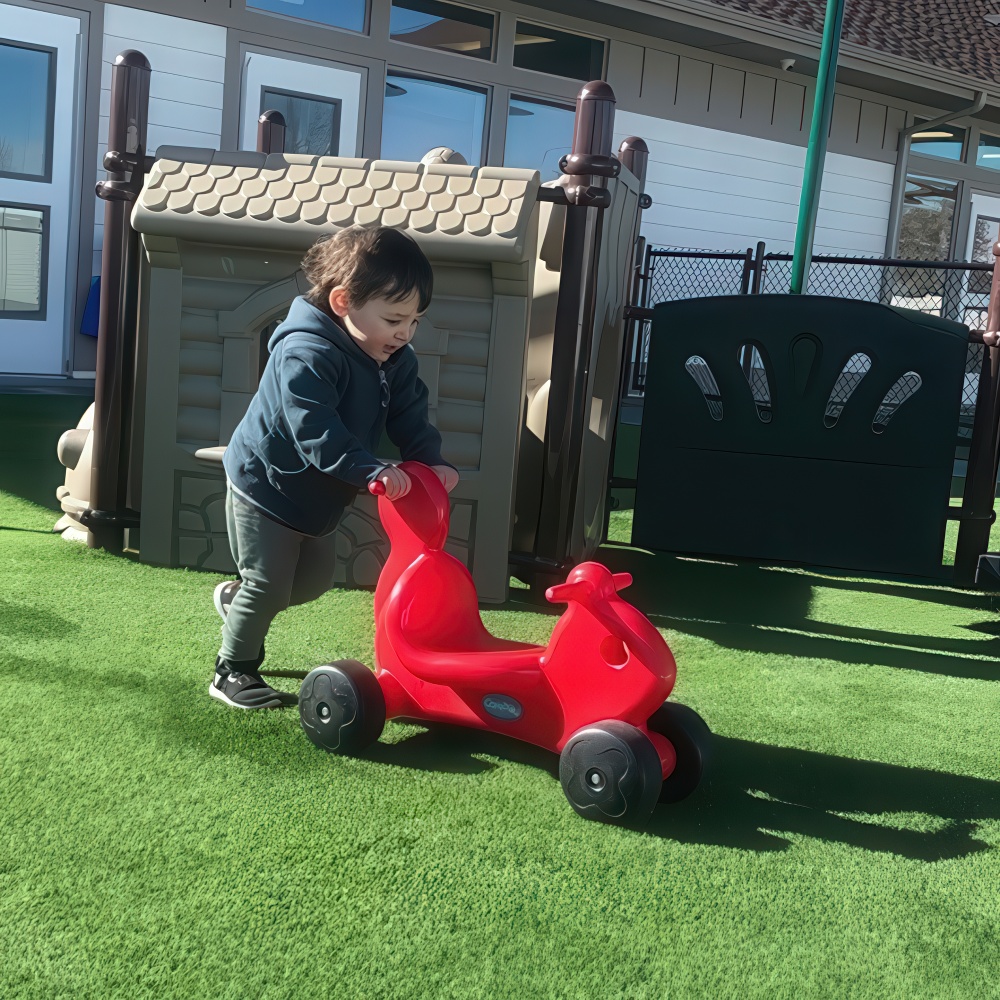 Toddler pushes a red scooter across the playground.