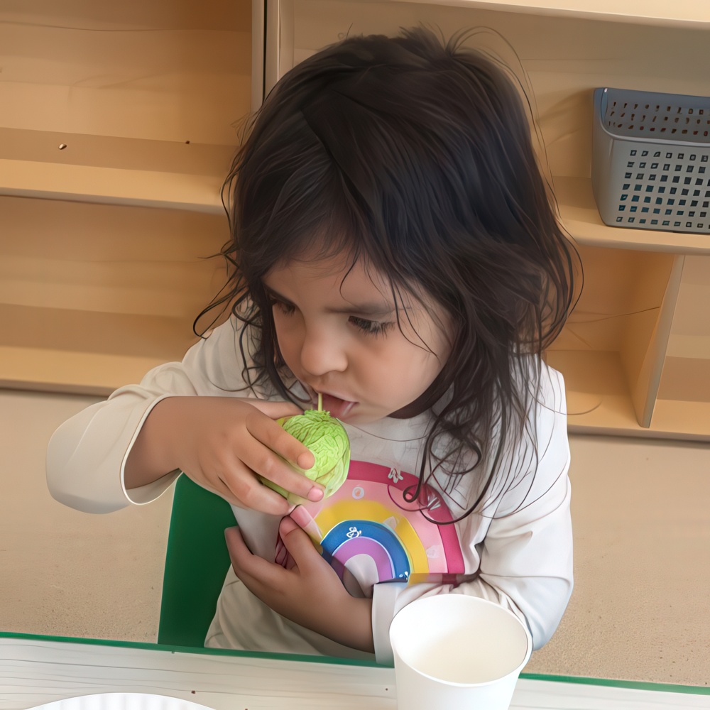 Young girl sipping from a cup with a rainbow shirt.