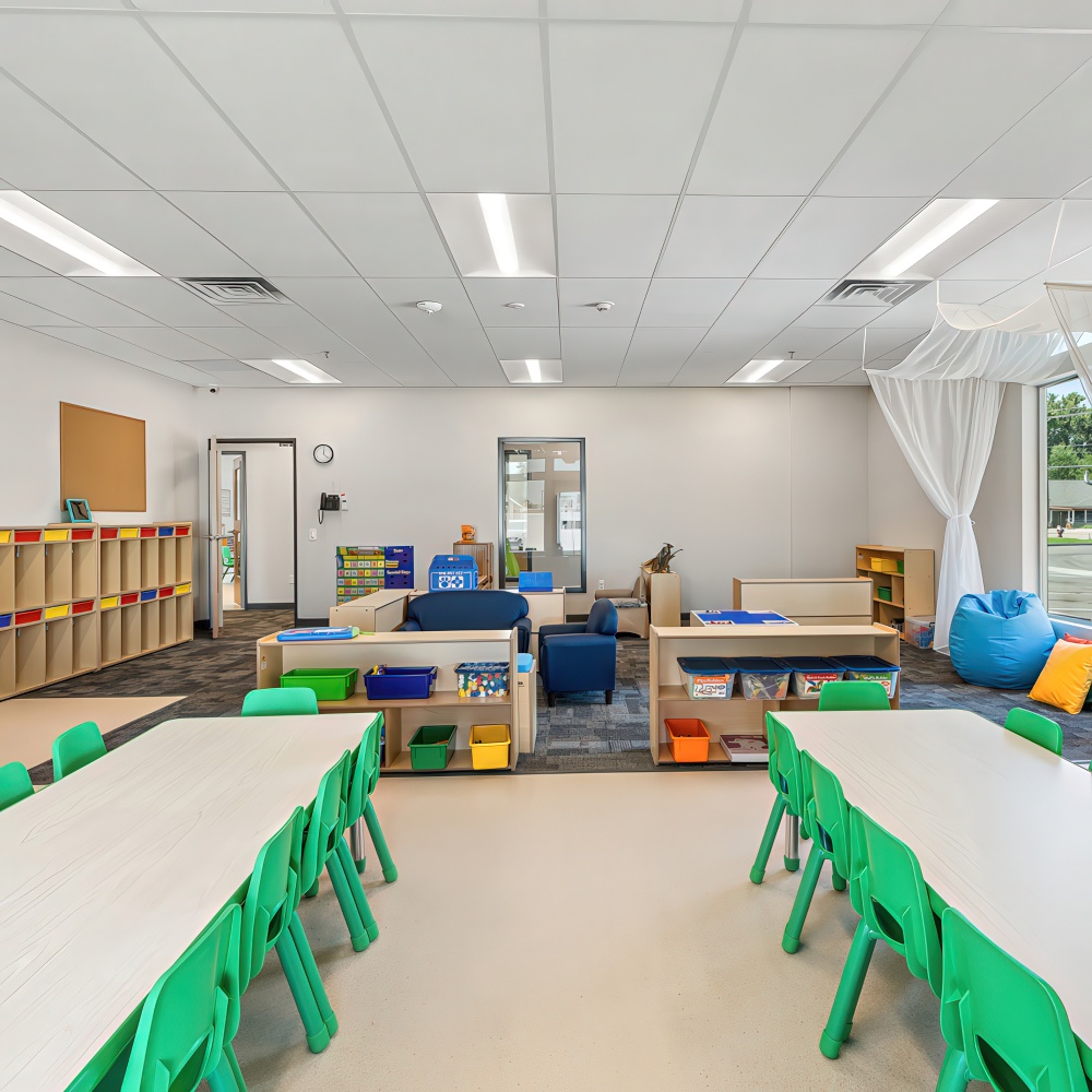 Classroom with multiple tables, green chairs, and cubbies.