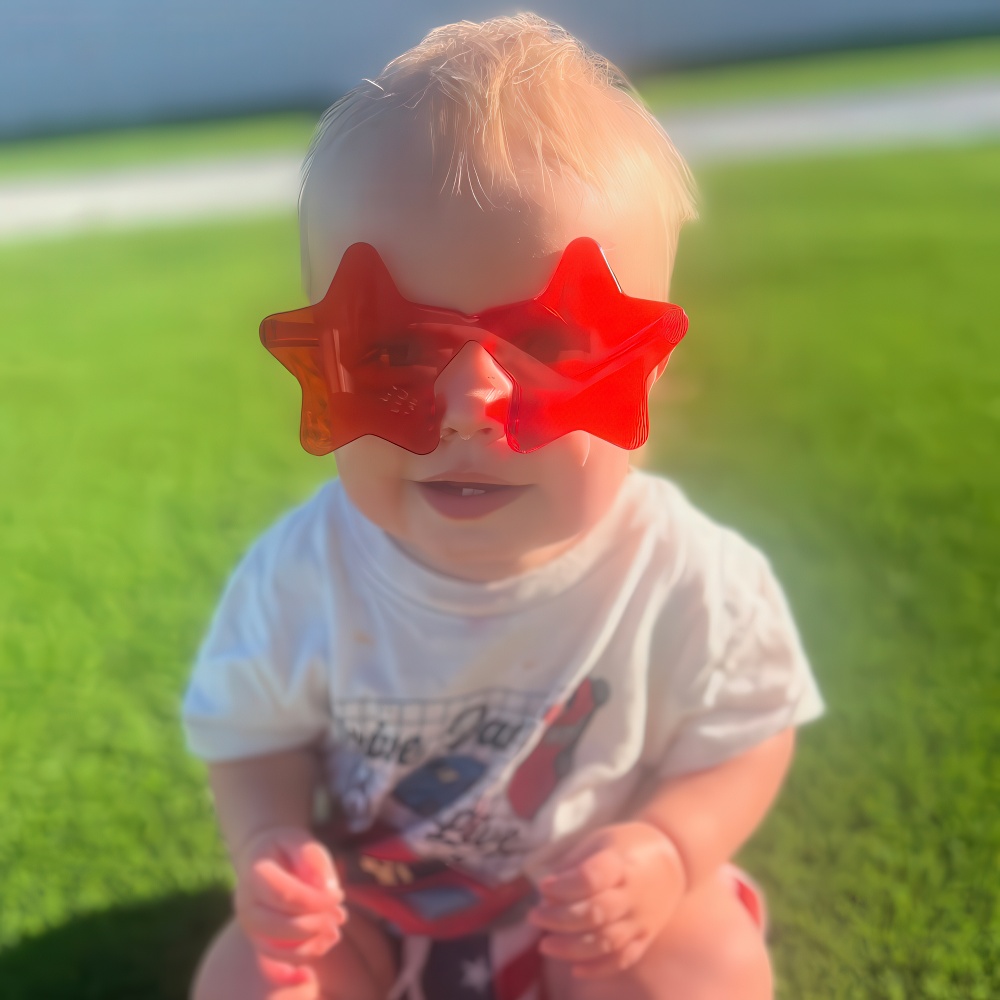 Baby outdoors in red star sunglasses, guided by teacher playtime.