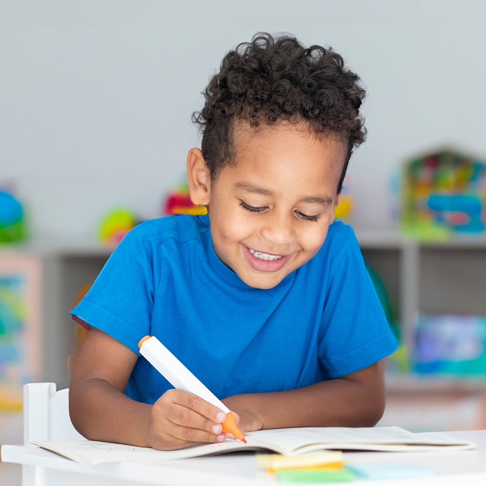 Smiling boy in blue shirt colors with an orange marker.