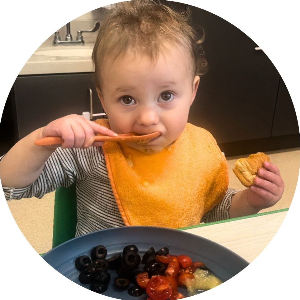 Toddler enjoys a healthy meal with fruits, olives, and bread.