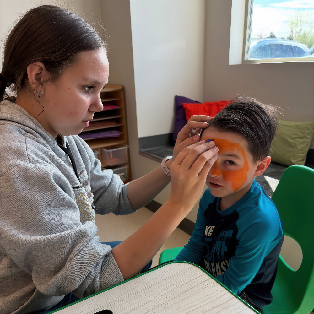 A teacher painting a child’s face during an indoor activity.