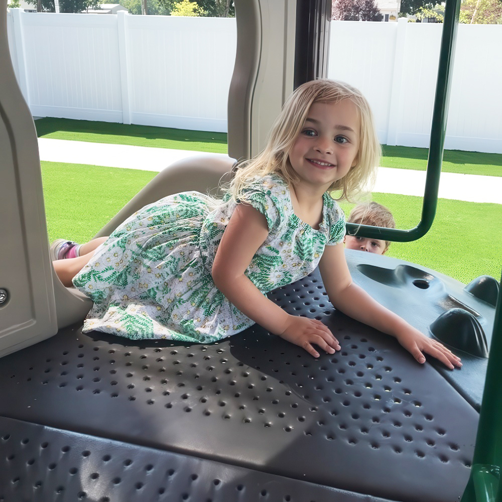 Girl smiles while climbing on outdoor playground equipment.