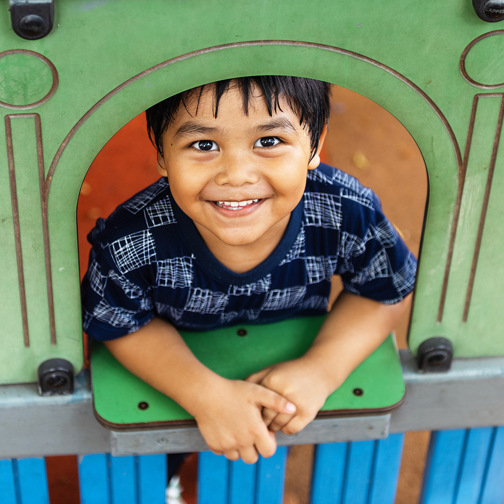 Smiling child peeks out from playground playhouse.