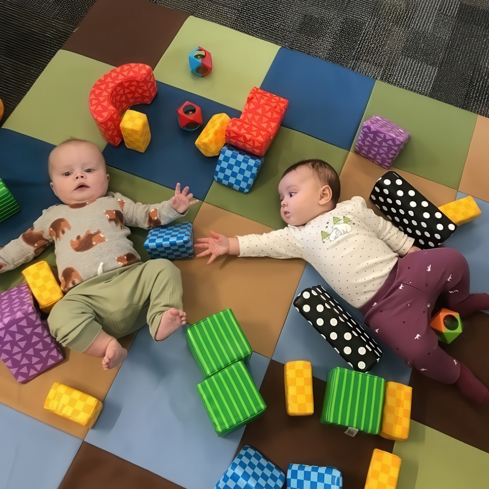 Infants on a play mat reaching for colorful blocks with teacher.